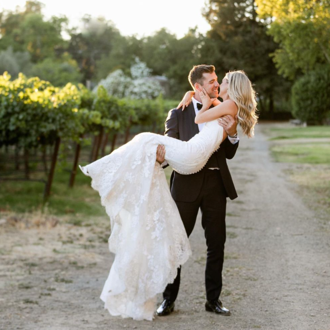 Groom lifting his bride along a Napa vineyard path at golden hour