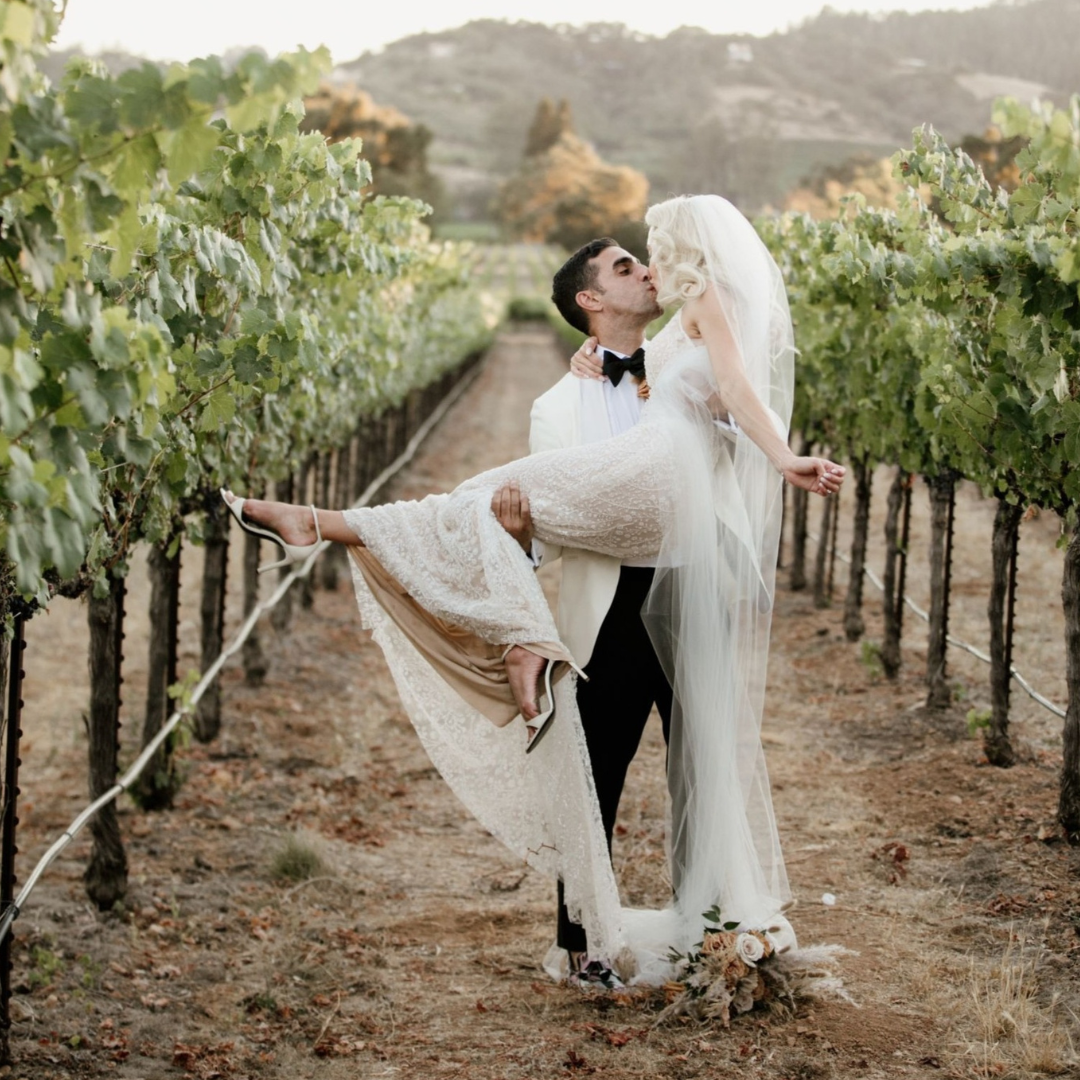 Groom lifting and kissing his bride between rows of Napa Valley vines